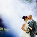 Bride and Groom kissing at West Mill Derby wedding with colour smoke and sunshine behind them